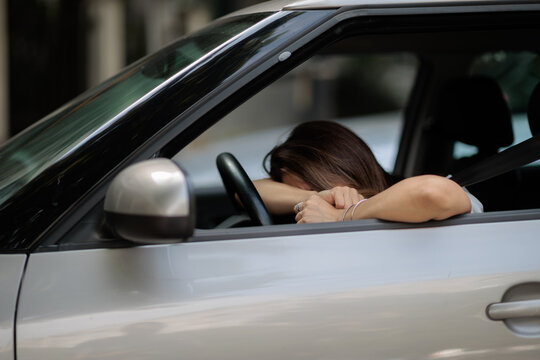 Desperate Crying Woman Leaning On Steering Wheel Inside Silver Car. Upset female driver hides face after mistake feeling depressed during traffic jam
