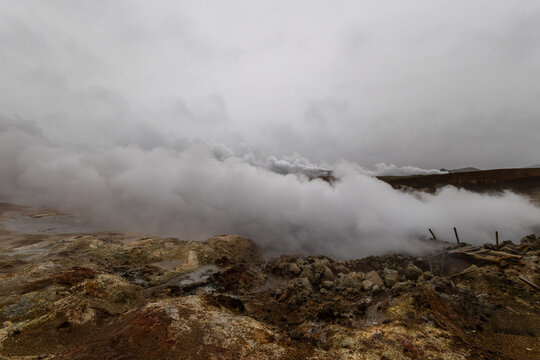 Thick steam rising from Gunnuhver geothermal hot spring past a damaged boardwalk under cloudy skies on Reykjanes Peninsula Iceland