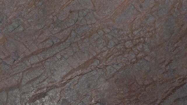 Close-up texture of a brown and grey natural rock surface with linear cracks and layered geological formations.