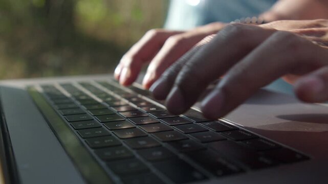 Close-up of a man's hands typing on a laptop while working outdoors in front of a camping tent, capturing remote work, outdoor workspace, and digital nomad lifestyle.