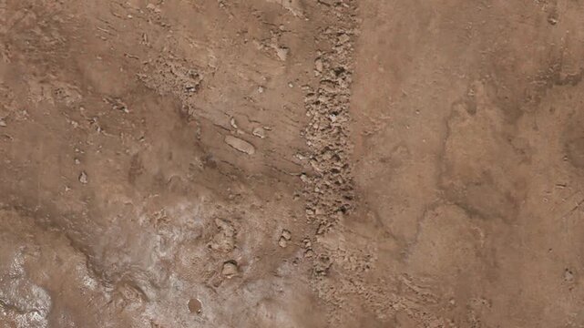 Top down view of wet, brown mud showing distinct tracks and uneven ridges. This rough terrain texture perfectly captures a messy, disturbed ground surface suitable for off-road or muddy concepts.