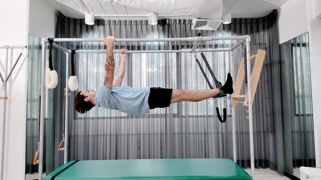 A person is doing exercises on a reformer in a fitness studio. The studio has gray curtains and a green exercise table. The workout focuses on strength and balance.