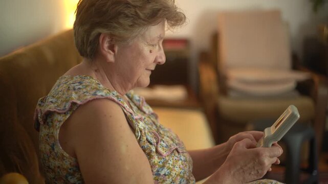 A retired senior woman at home playing a portable video retro game console and having fun