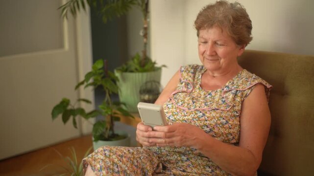 A retired senior woman at home playing a portable video retro game console and having fun