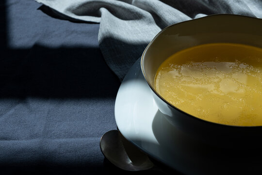 Bowl of freshly prepared collagen-rich beef bone broth with greens on a linen tablecloth