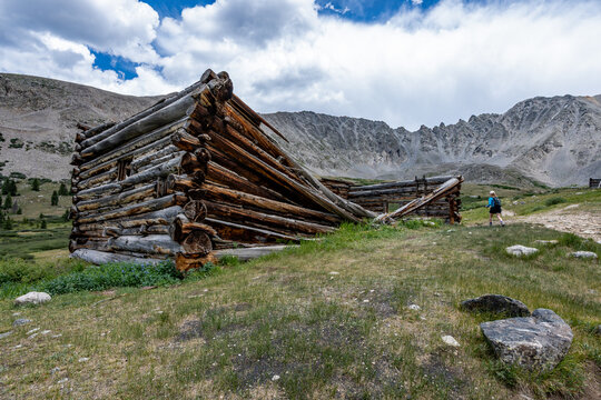 Woman hiker exploring abandoned mining cabins on Mayflower Gulch trail near Copper Mountain, Colorado under summer afternoon cloudscape.