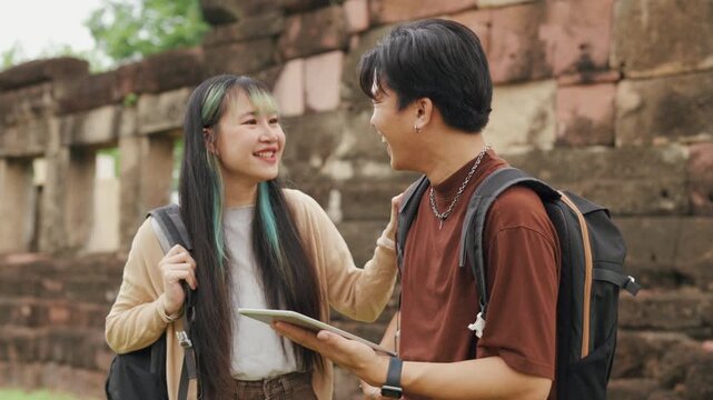 Happy young Asian couple exploring ancient temple ruins with map and smartphone during summer travel vacation. Cheerful romantic tourist lovers enjoying historic sightseeing adventure.