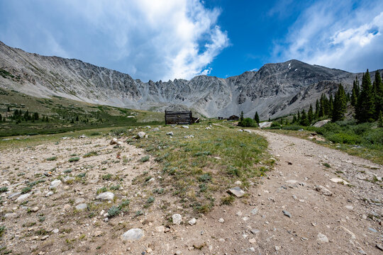 Ruins of former mining cabins on Mayflower Gulch Trail near Copper Mountain, Colorado under summer afternoon cloudscape.