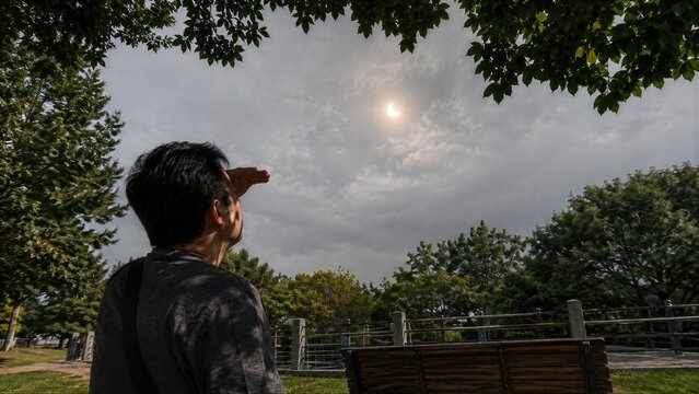 Man Shields Eyes While Looking at Partial Solar Eclipse Through Clouds