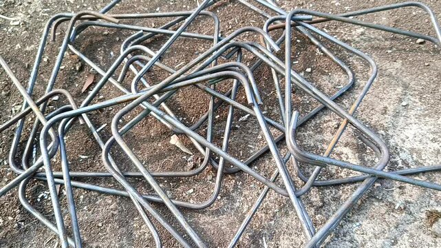 Slow camera movement over scattered rebar stirrups and steel rings for building construction framework.