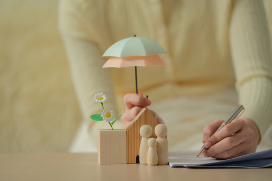 Home insurance concept, woman holding umbrella over miniature house and flowers for property protection, home insurance, safety, coverage, security, protection