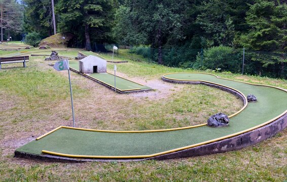 miniature golf course with relaxed recreational activities in a scenic park with green grass and brown trees under natural light and concrete structures, aerial view of holes and turf.