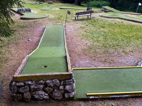 miniature golf course with relaxed recreational activities in a scenic park with green grass and brown trees under natural light and concrete structures, aerial view of holes and turf.