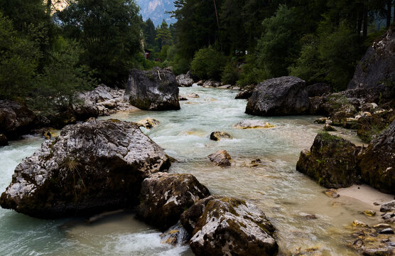 serene river flowing around rocks in natural landscape with trees and rocks above the riverbed. green and brown environment with blue water and gray rocks, peaceful nature.