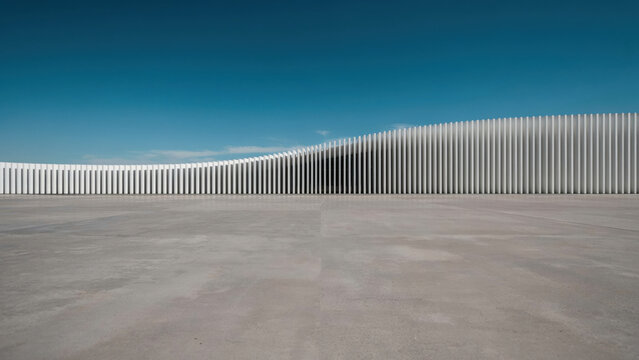 Minimalist architectural facade with a curved wall and empty concrete plaza under a clear blue sky.