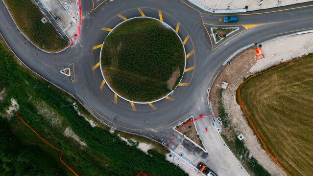  aerial view of urban roundabout with roads and green spaces in neutral setting, showing asphalt, grass, and concrete materials under natural light.