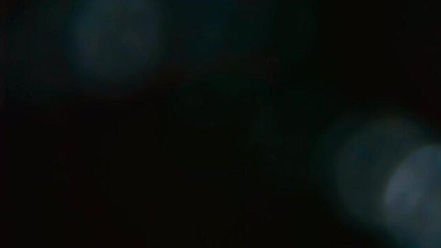 Abstract dark background with soft glowing bokeh light flares.