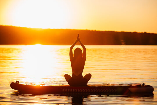 Woman practicing yoga on sup board at sunset