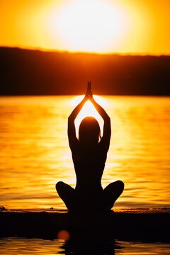 Woman meditating on paddleboard during golden sunset