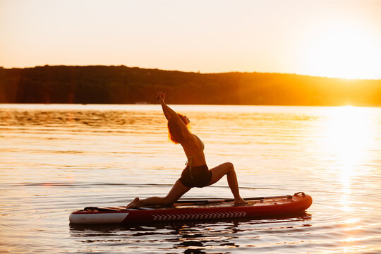 Woman practicing sup yoga during sunset
