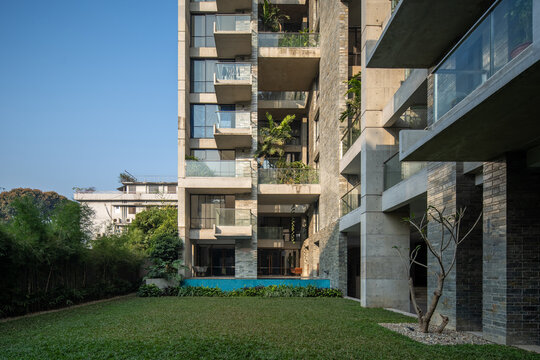 Modern Residential Building with Glass Balconies, Stone Facade, Green Lawn, and Outdoor Garden