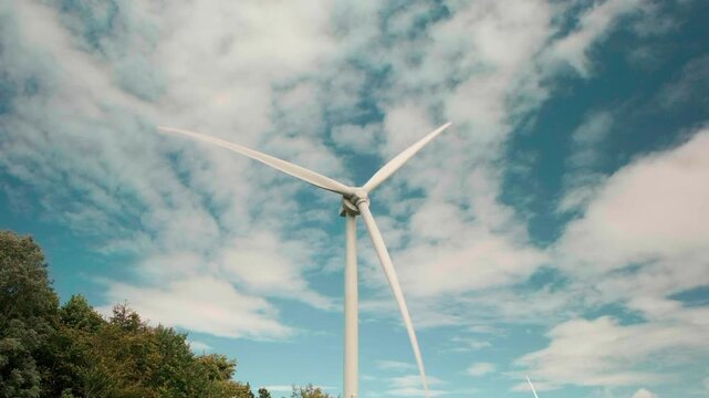 Wind turbine stands tall against a sky filled with clouds. Trees frame the base of the structure. The scene radiates clean, renewable energy. Ideal for environmental or sustainability projects