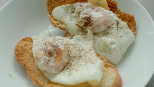Two fried eggs rest on toasted bread slices. White plate holds simple, warm breakfast dish. Slight seasoning dusts the soft whites. Comforting, home-style meal idea. Perfect for food, cooking