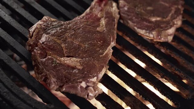 Close up of marbled steaks sizzling on a hot grill with flames and charred marks