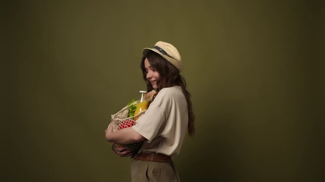 Happy young woman holding reusable mesh bag with fresh organic groceries and smiling at camera