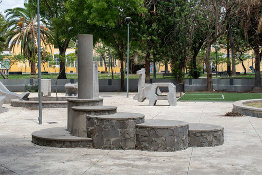 Guadalajara, Mexico - June 14 2025: Concrete play sculptures and circular stone seating in Parque Morelos, Guadalajara, with trees and yellow buildings in background