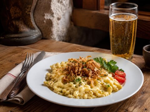 K&auml;sesp&auml;tzle mit R&ouml;stzwiebeln im deutschen Restaurant &ndash; deutscher Klassiker aus S&uuml;ddeutschland, cremig mit geschmolzenem K&auml;se und herzhaft auf wei&szlig;em Teller serviert.