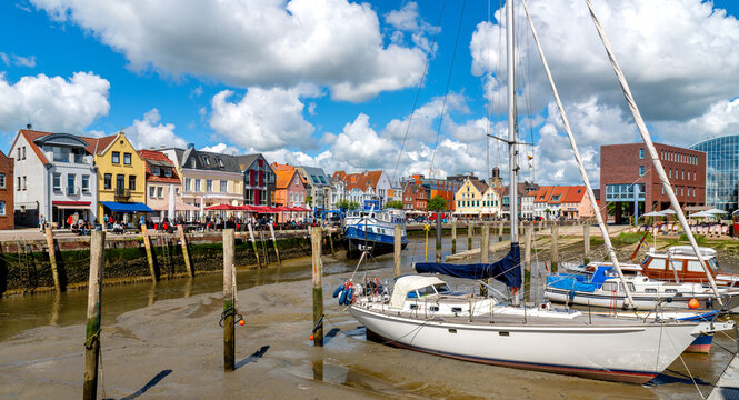 The historic harbor of Husum at low tide. Sailing yachts rest on the exposed harbor floor while the colorful old town forms the backdrop.