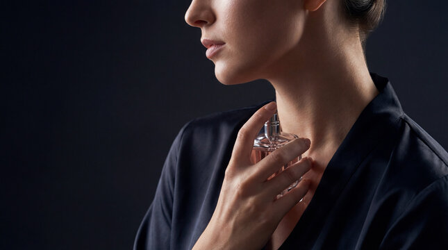 Elegant woman applying perfume near neck in dramatic close up portrait conveying beauty ritual personal fragrance luxury self care sophistication confidence sensual style copy space