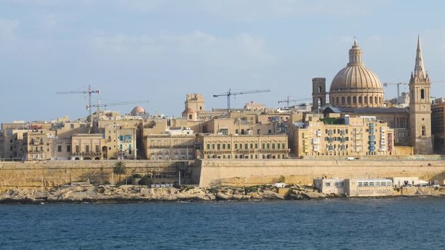 wide golden hour view of the valletta skyline warm evening light glowing across the dome and spire silhouette carmelite church dome st pauls anglican cathedral baroque skyline malta capital city