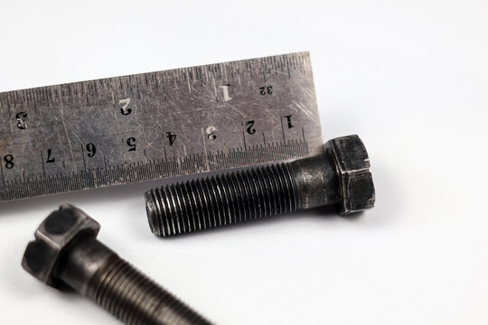 Measuring black steel hex bolts with steel ruler isolated on white background.