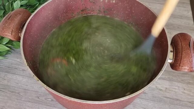 Top view of traditional Egyptian molokhia soup cooking in a copper pot. Fresh green molokhia leaves with garlic and coriander being stirred with a wooden spoon. Steam rising from the hot soup. Authent