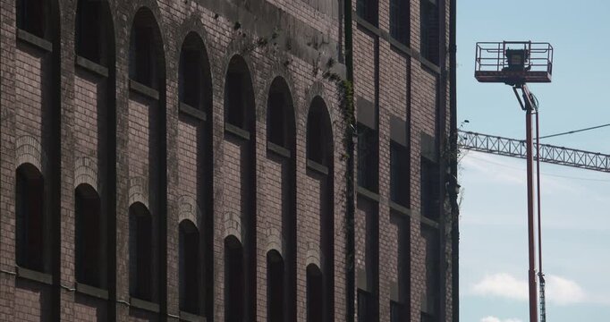 Old red brick derelict building facade with construction crane platform in background