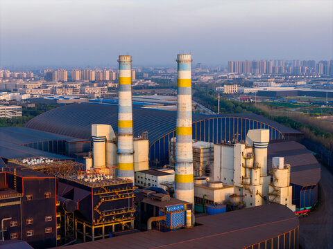  Industrial chimneys of a power plant at dusk over urban skyline