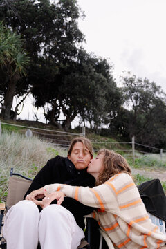 UGC Friend kissing woman on beach chair during autumn afternoon