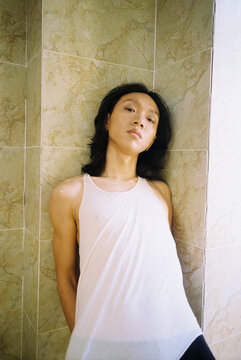 Young Man Leaning Against Tiled Wall in Wet Tank Top