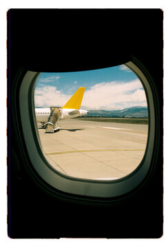 A yellow-tailed plane on the tarmac seen through a cabin window