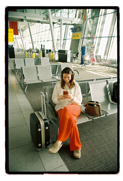 A woman scrolls her phone at an airport departure gate