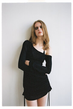 Model poses in a black dress against a light wall in a studio
