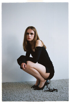 Woman squatting in a black dress and high heels