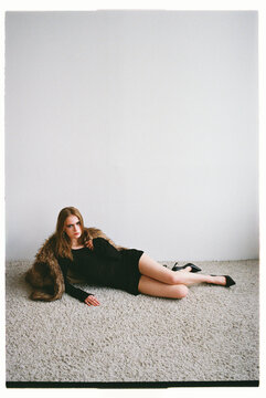 Model poses on the floor wearing a black dress and a fur coat