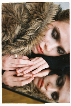 Woman with fur coat resting her head on hands on mirror reflection