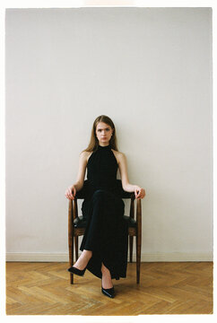 Model sits in a chair in a simple room with plain walls
