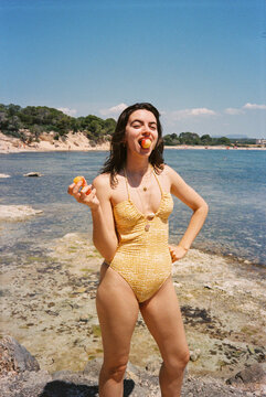 Woman Standing by the Water at the Beach Holding Fruit
