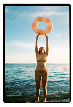 A woman lifts a pink pool ring above the open sea