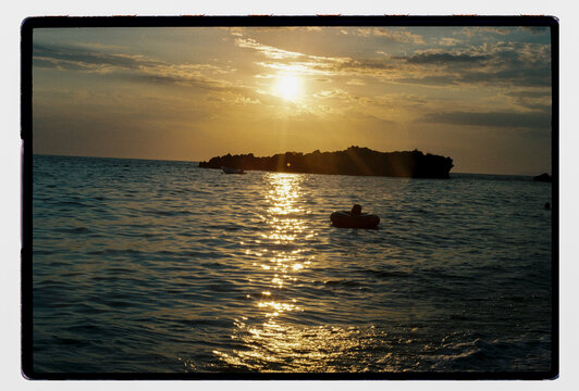 A person floats on an inner tube as the sun sets over the sea